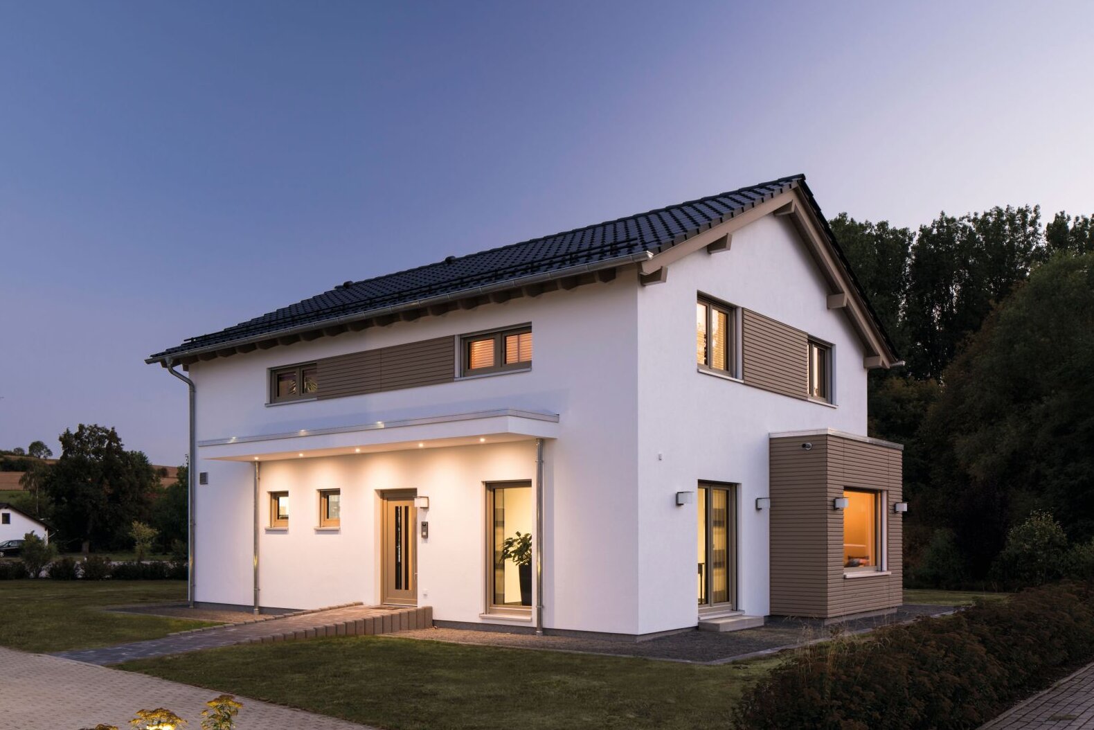 Musterhaus SENTO von FingerHaus in Frankenberg, zweigeschossiges Einfamilienhaus mit Satteldach, weißer Putzfassade, horizontalen Fensterelementen, überdachtem Eingangsbereich und beleuchtetem Innenraum in der Dämmerung.