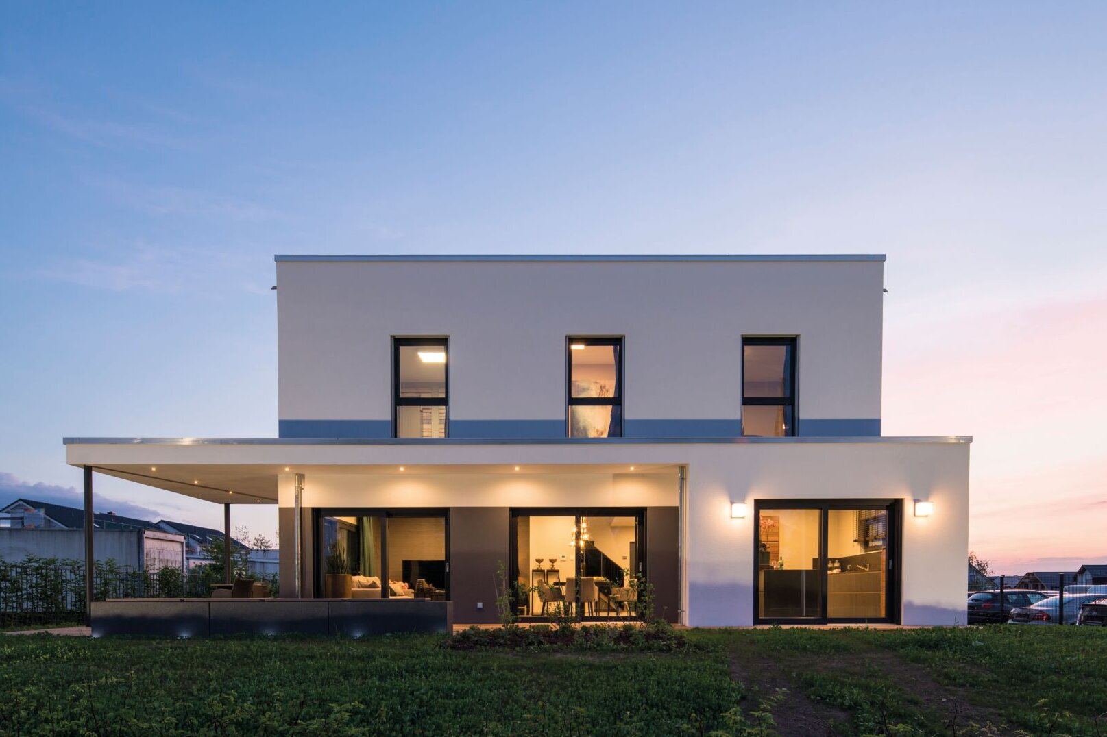 Außenansicht des FingerHaus Musterhauses ALTERO in Gießen bei Sonnenuntergang mit moderner kubischer Architektur und überdachter Terrasse.