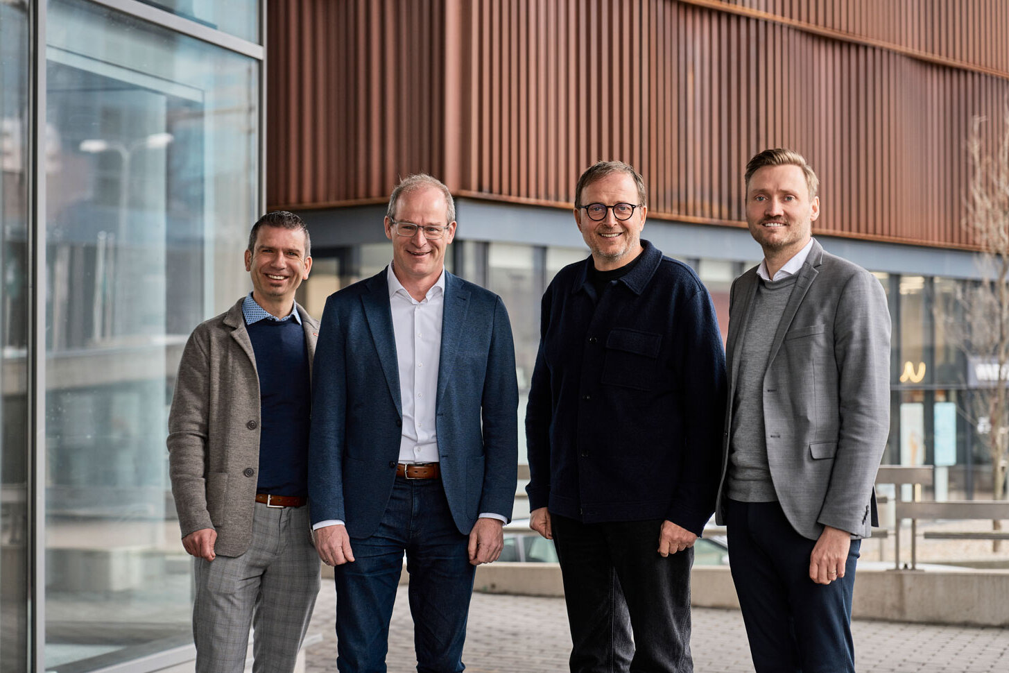 Vier Personen stehen vor einem modernen Bürogebäude mit Glasfassade und Holzlamellenfassade. Von links nach rechts: Jan Wegner (VELUX), Dr. Mathias Schäfer und Klaus Cronau (FingerHaus Geschäftsführung) sowie André Osterhoff (VELUX).