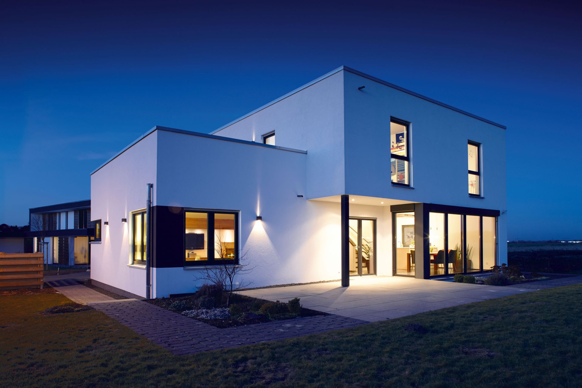 Modernes, kubisches Fertighaus von FingerHaus mit großen Fenstern und Außenbeleuchtung bei Dämmerung